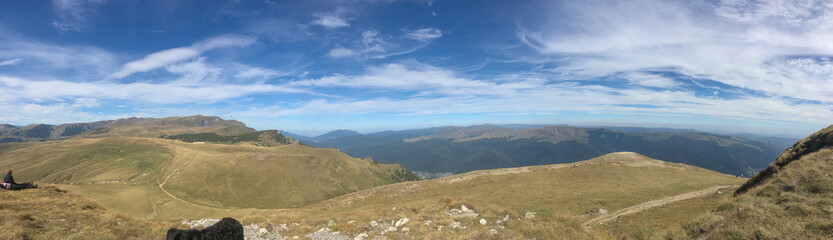 Fototapeta premium Panoramic view over a mountain range with a valley in summer and resting hikers