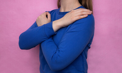 The girl in a blue sweater hugs herself on a pink background. Concept for March 8th, #IWD2023,...