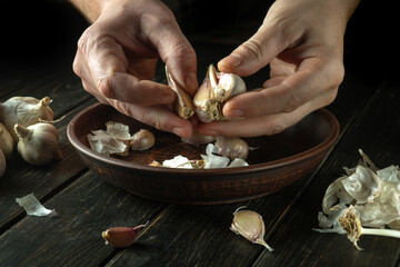 Close-up of a cook hands peeling garlic in the kitchen. The concept of cooking vegetarian food on a dark background