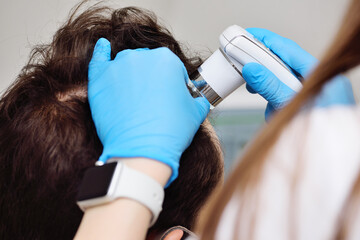 Close-up cosmetologist trichologist diagnoses the condition of the hair of a male patient with...