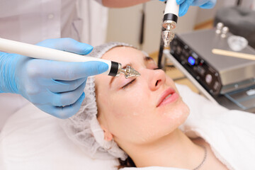 cosmetologist conducts microcurrent facial therapy for a young woman using a device in a beauty...