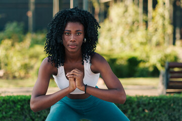 bella mujer negra con ropa deportiva, preparándose para hacer ejercicios, haciendo estiramiento, sentadillas y flexiones, corriendo en un parque con luz natural.	