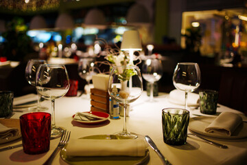 a table with a white tablecloth, glasses, crockery and decor in dark restaurant