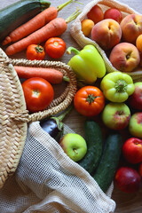 Straw bag and reusable fabric bags filled with various healthy fruit and vegetables. Wooden background, top view.