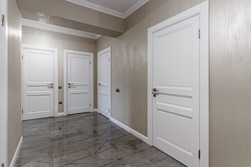 Corridor with white walls and doors in an apartment with a marble floor