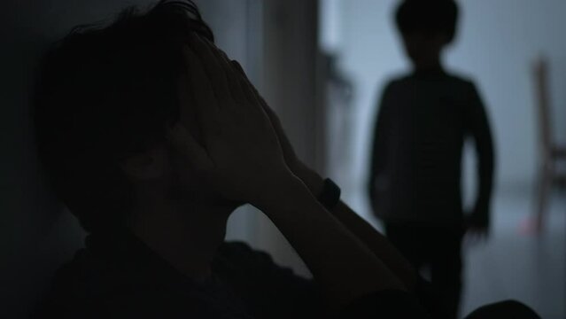 Sad father being held by son. Dramatic scene of male parent suffering sitting in corridor in the dark. Child consoling dad