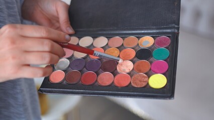 Makeup artist holds shadows in his hand and paints a model.