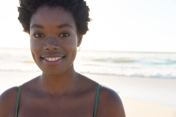 Close-up of smiling african american young woman with afro short hair over sea and sky at sunset