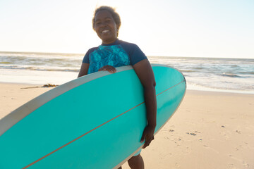 Fototapeta premium Senior african american senior woman with surfboard enjoying on sandy beach against sea and sky