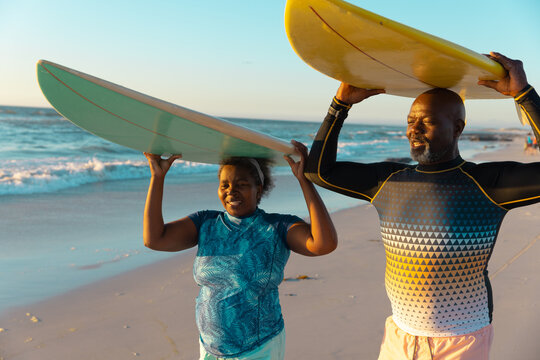 African american senior couple carrying surfboards on heads while standing at beach against sky