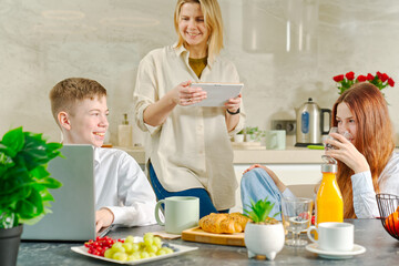 Obraz na płótnie Canvas Young family with school kids have fun at breakfast time. Happy family eating healthy breakfast. Quality time with Family in kitchen eating together. Family Using Digital Devices At Breakfast