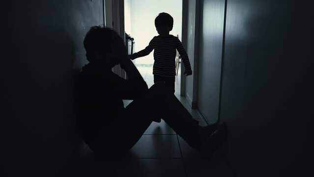 Depressed father being consoled by son sitting in corridor in silhouette. Child hugging sad parent during crisis