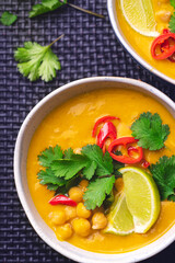 Light orange veggie curry with chickpeas, chili peppers, coriander leaves and cumin seeds on a wicker ethnic tray. Vegetarian recipes, healthy food Fusion cuisine, close up