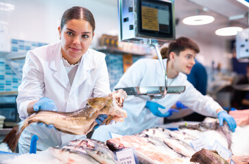Portrait of saleswoman offering fresh fish atlantic cod at seafood shop