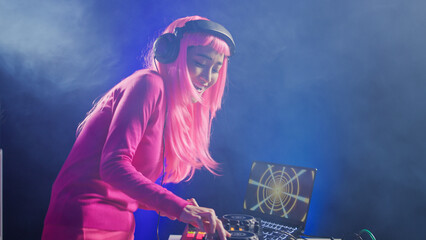 Smiling artist standing at dj table playing electronic music at professional mixer console in...