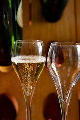 Glasses of sparkling white wine champagne or cava with bubbles and classic wooden champagne pupitre rack with empty bottles on background
