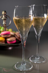 Glasses of sparkling white wine champagne or cava with bubbles and sweet dessert colorful macarons biscuits on background