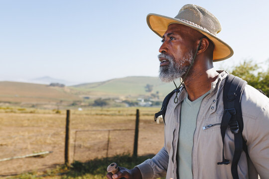 Bearded african american senior man wearing hat looking away while hiking on land against clear sky