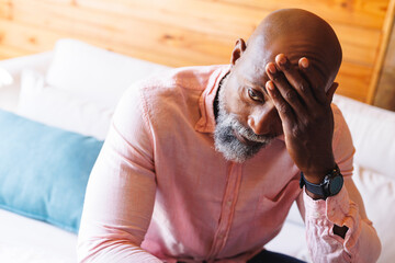 Close-up of stressed bald african american senior man with head in hand sitting on sofa in log cabin