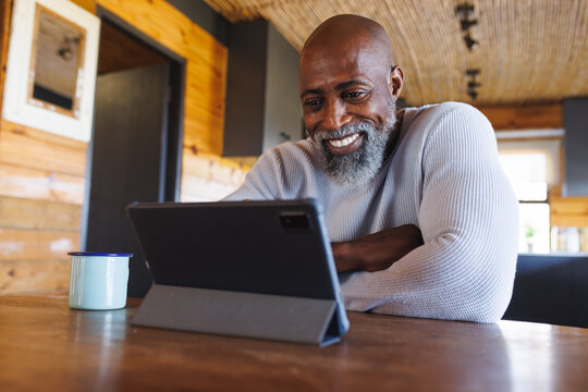Smiling bald african american senior man talking on video call over digital tablet in log cabin