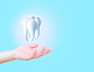 The hand holds a molar tooth on a light blue background, dental examination, dental health and...
