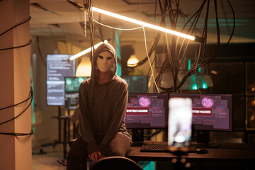 Obraz na płótnie Canvas Anonymous hacker attacking database server portrait, cybercrime. Computer system hacking, information phishing, malware programming, cyber criminal in mask looking at camera at night time