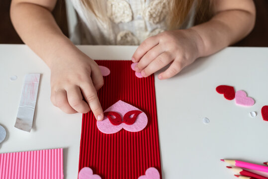 Child's hands making of handmade Valentine's day cards using color paper and felt. Children's DIY holiday card, gift for Mother's day, Father's day, hobby, crafts concept.