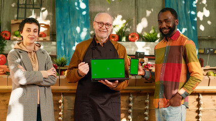Diverse group of people showing greenscreen on laptop and smartphone, holding devices with isolated chrom key display. Farmer and clients using blank mockup template and copyspace screen.