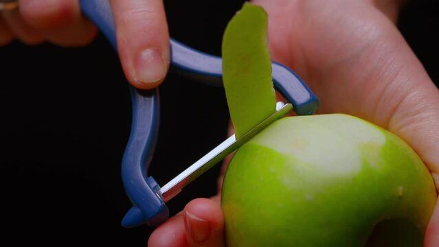 a green apple is peeled with a special knife on a black background.Apple in the cook's hand. High quality 4k footage