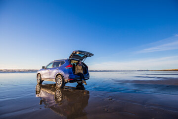 View of young woman traveler sitting on suv car  on the Delaura Beach in Oregon. Photo with the...