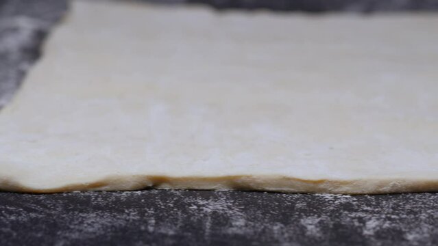 a panorama of spread dough on a black table with flour and a kitchen rolling pin is placed on the table. slow motion