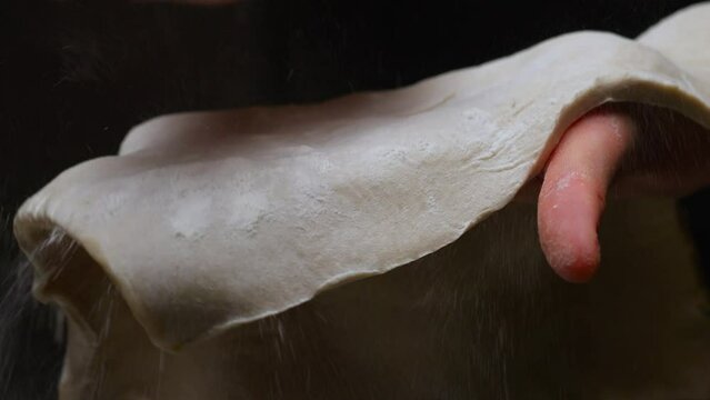 the hands of the cook prepare the dough and sprinkle flour on it. filmed on a black background, slow motion