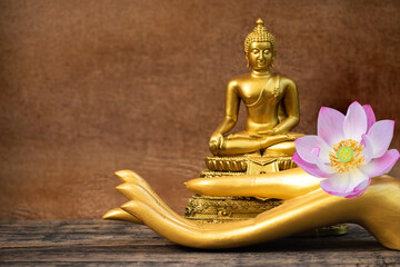 Buddha statue and golden hands on an old wooden background.