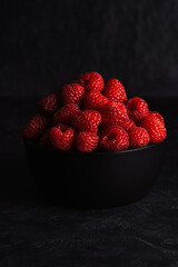 Ripe raspberries in black bowl on  dark background.