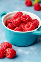 Fresh raspberry fruits in blue bowl, blue background
