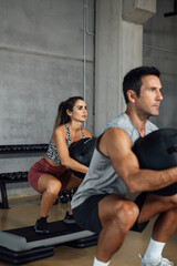 Sporty man and woman doing squats with fitness ball in the gym.