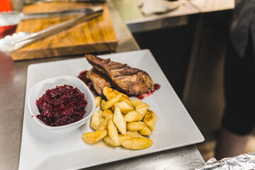 Unrecognisable person plating duck fillet with potato dumpling and red beetroot salad. Polish cuisine. Restaurant food plating process. Horizontal indoor shot. High quality photo