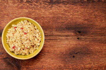 salad of couscous, spices and tomato tabbouleh in a yellow plate on a wooden background.