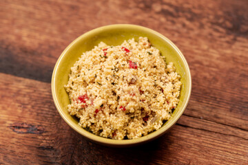 salad of couscous, spices and tomato tabbouleh in a yellow plate on a wooden background.