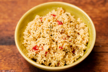 tabbouleh salad of couscous, spices and tomato - in a yellow plate on a wooden background. Traditional oriental salad, appetizer.