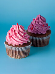 cupcake with strawberry cream and sprinkle of hearts and cupcake with blackcurrant cream and sprinkled with hearts on blue background macro close up vertical