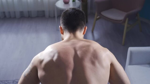 Man develops back muscles using equipment at home.
Young athlete man building back muscles by hugging barbell at home.

