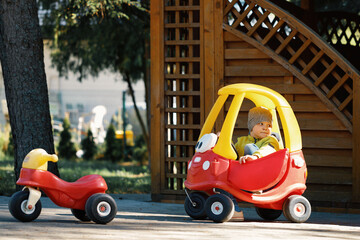 Portrait of cute little caucasain toddler boy enjoy having fun riding toy car in city park at spring day.