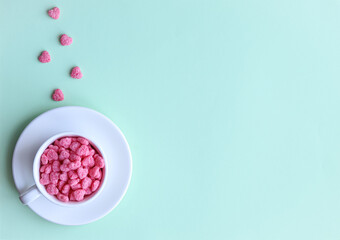 Cereal in the form of hearts lies in a white cup, which stands on a white saucer on a green background. Valentine's day concept. Copy space.