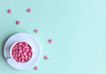 Cereal in the form of hearts lies in a white cup, which stands on a white saucer on a green background. Valentine's day concept.