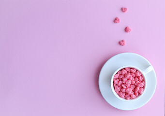 Cereal in the form of hearts lies in a white cup, which stands on a white saucer on a pink background. Valentine's day concept. Copy space.