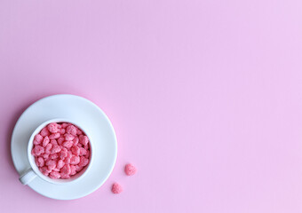 Fototapeta na wymiar Cereal in the form of hearts lies in a white cup, which stands on a white saucer on a pink background. Valentine's day concept.