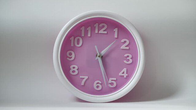 Portrait of clock isolated on a white background with a pink dial and white numerals. The concept of time clock is depicted. The hands of the clock move smoothly showing the transience of time