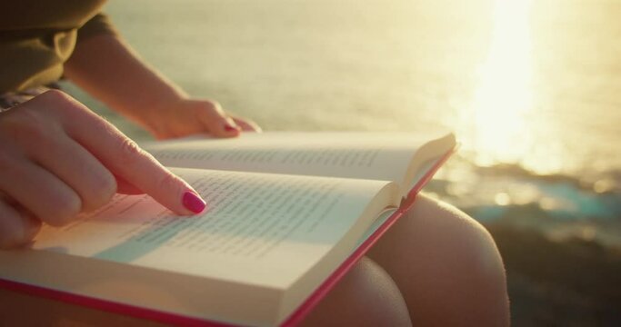 Woman reading red book on beach at sunset light. Learning, studying, education concept.