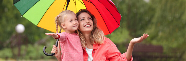 Happy mother and daughter with bright umbrella under autumn rain outdoors. Banner design
